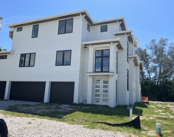 White three-story modern house with sand finish stucco, black window frames, large glass front door, and a three-car garage